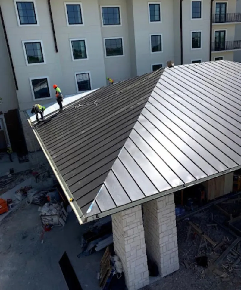 Crew installing standing seam metal roof panels on a commercial project in Denton